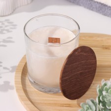 A candle made of soy wax in a glass with a wooden wick and a lid 