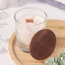 A candle made of soy wax in a glass with a wooden wick and a cover 