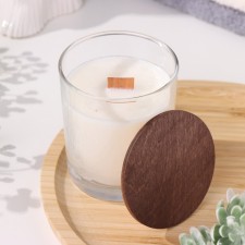 A candle made of soy wax in a glass with a wooden wick and a lid 