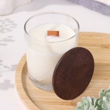 A candle made of soy wax in a glass with a wooden wick and a lid 